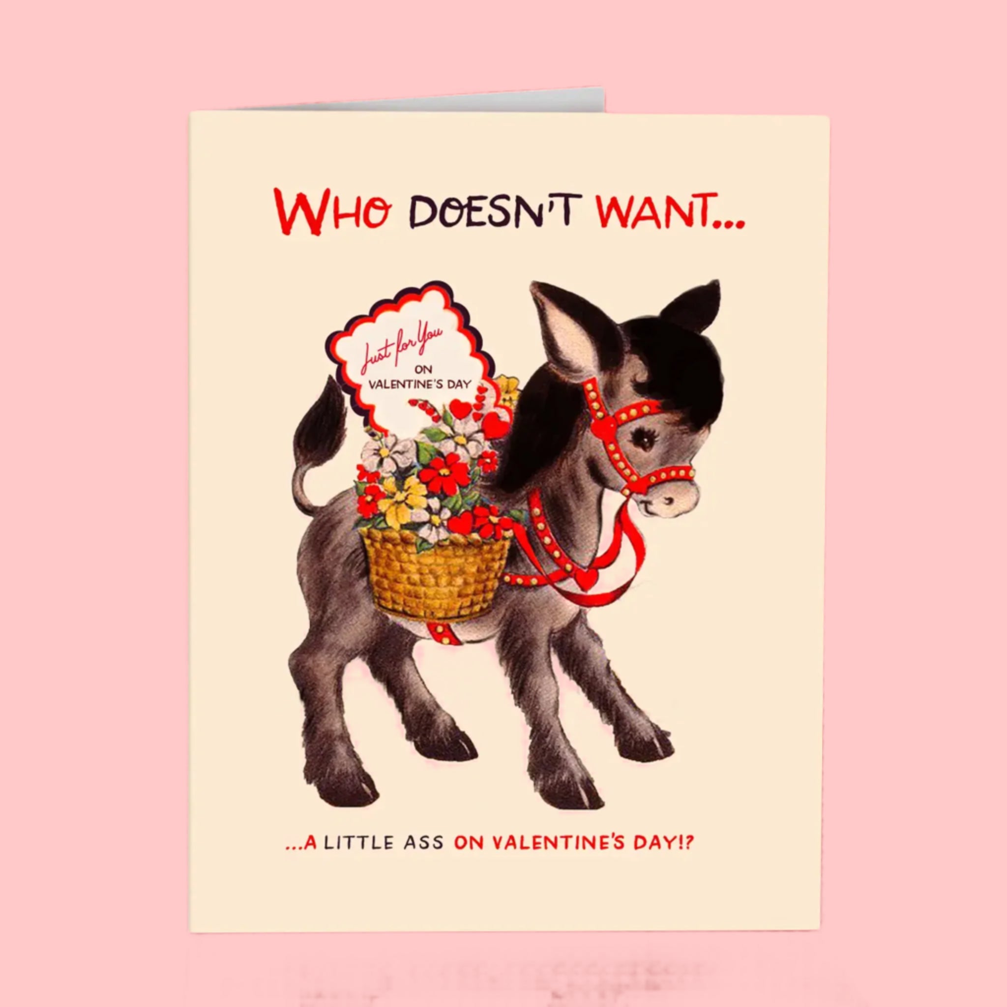 A cream card with an illustration of a donkey with flowers and its back and text above and below that reads, &#39;Who doesn&#39;t want... ...a little ass on Valentine&#39;s Day?!&#39;. 