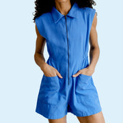 A model wearing a French blue jumpsuit with no sleeves, a collar, front pockets and a zipper. 