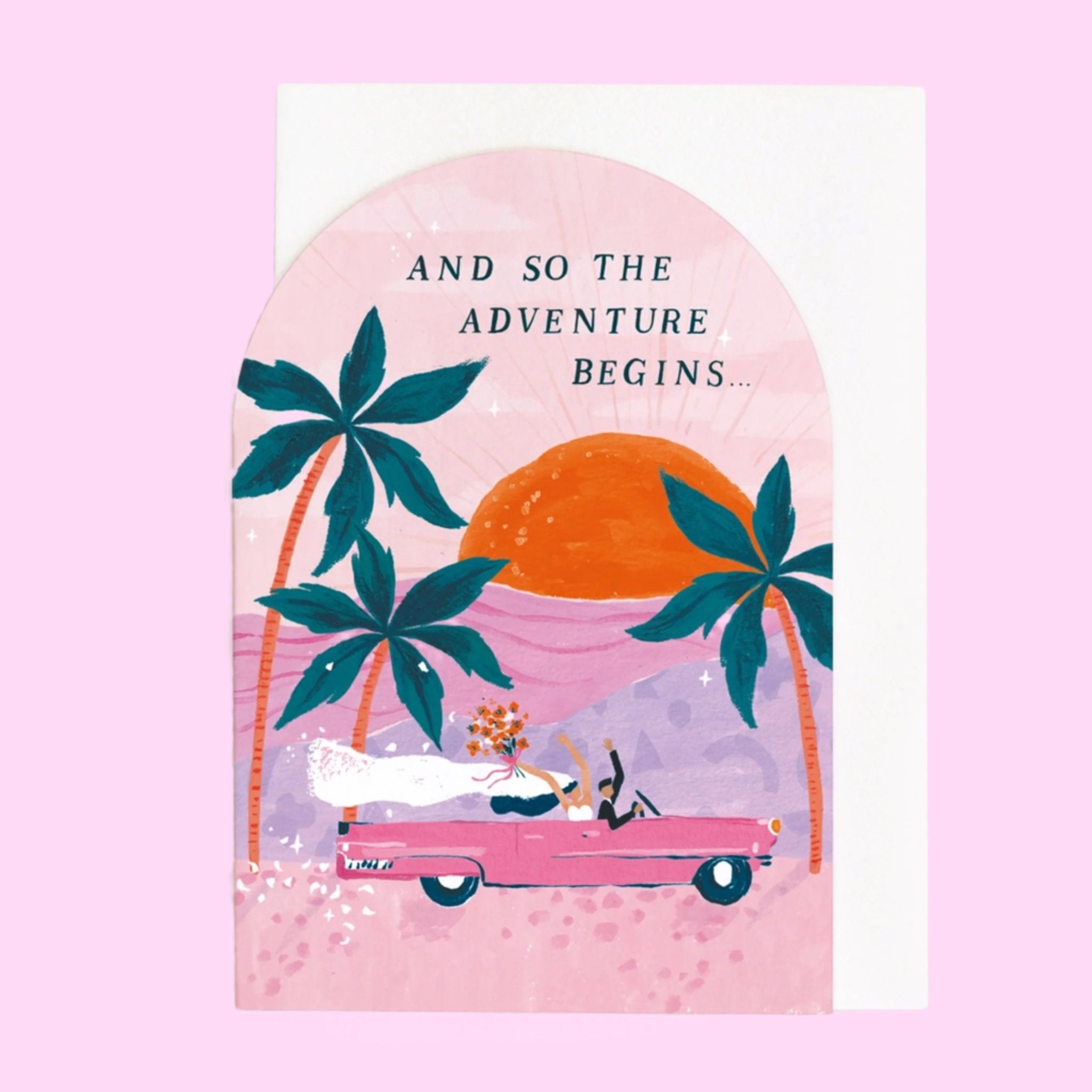 A pink arched greeting card featuring three palm tree illustrations along with a pink vintage car riding into the sunset with a bride and groom holding their hands and bouquets in the air as well as text that reads, &quot;And So The Adventure Begins...&quot; in black letters.