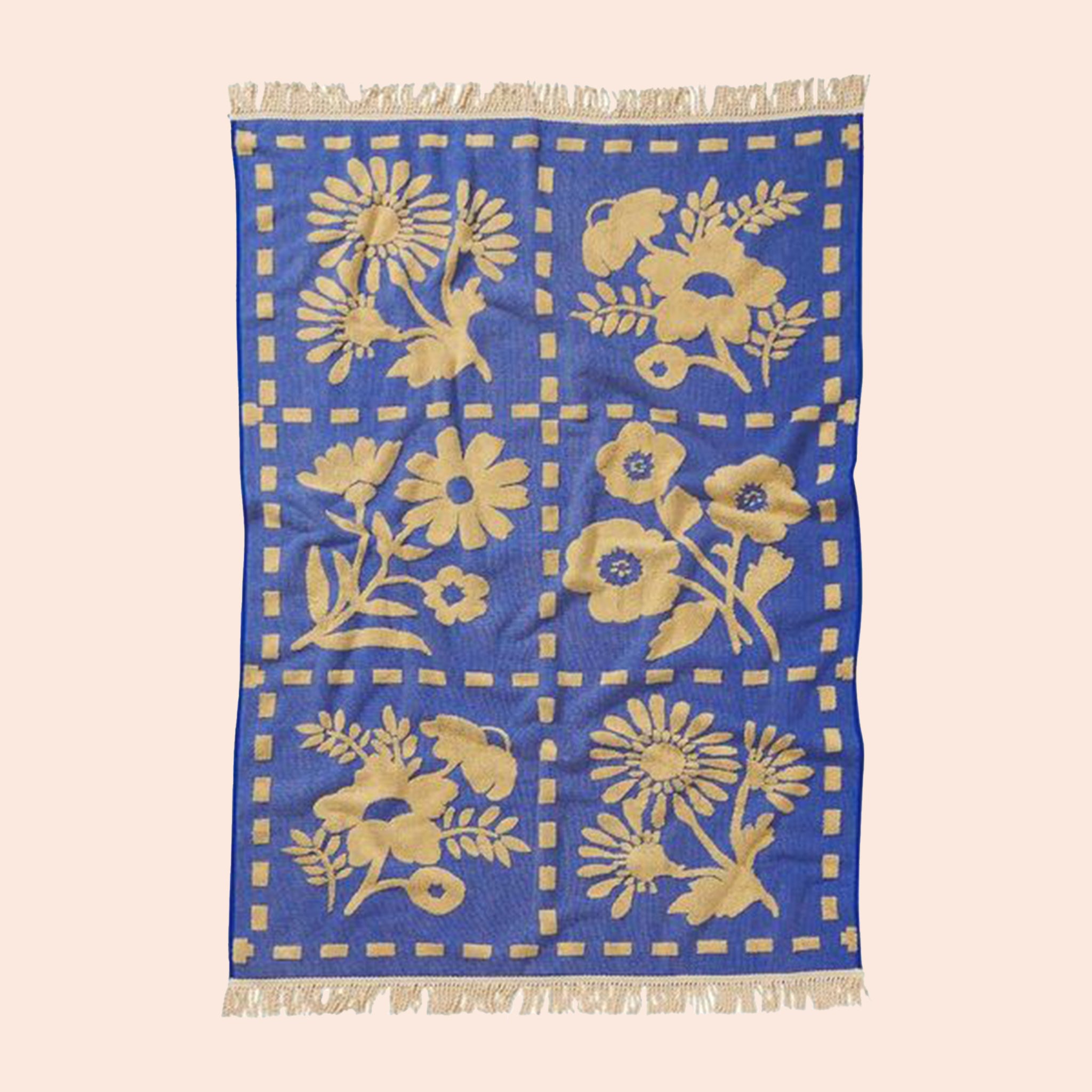 A blue and cream floral pattern bath towel with fringe detailing on two ends. 