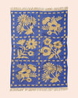 A blue and cream floral pattern bath towel with fringe detailing on two ends. 