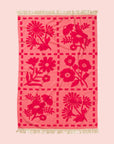 A pink bath towel with a floral print and fringe details on two edges. 
