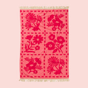 A pink bath towel with a floral print and fringe details on two edges. 
