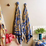 A blue and cream floral pattern bath towel with fringe detailing on two ends. 