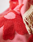 A light and dark pink hand towel with a floral pattern and fringe detailing on two ends. 