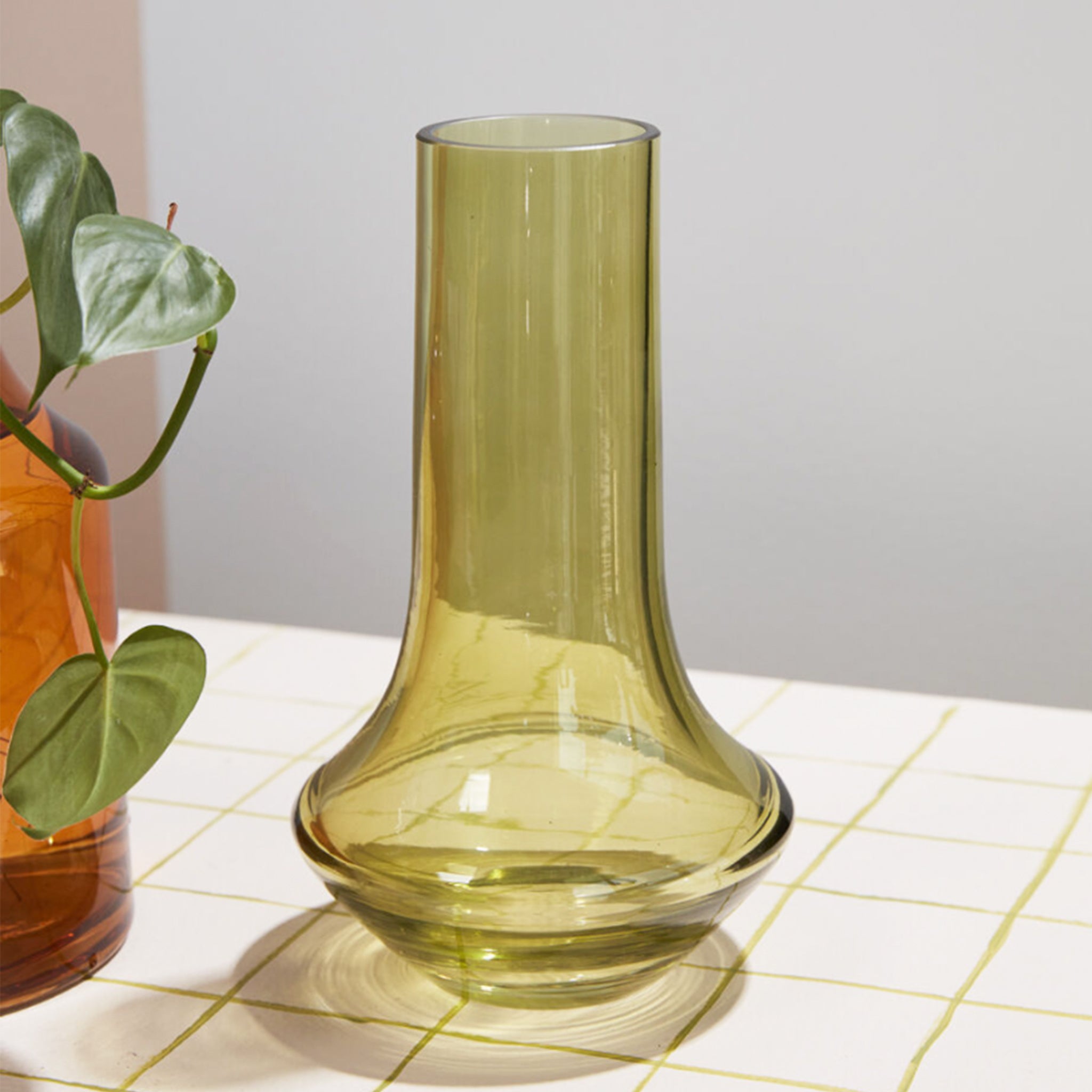 A glass green vase with a bottle neck and wide base. 