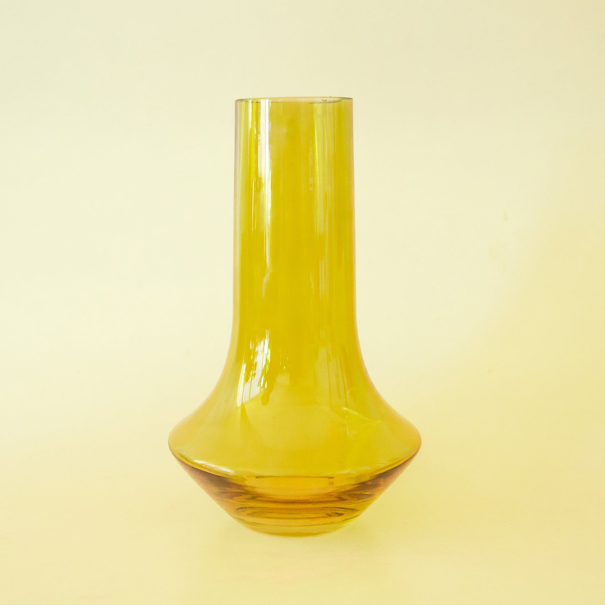 A glass green vase with a bottle neck and wide base. 