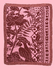 On a pink background is a pink and rust tropical print with "sage x clare" down the side of one edge along with fringe edges on all sides. 