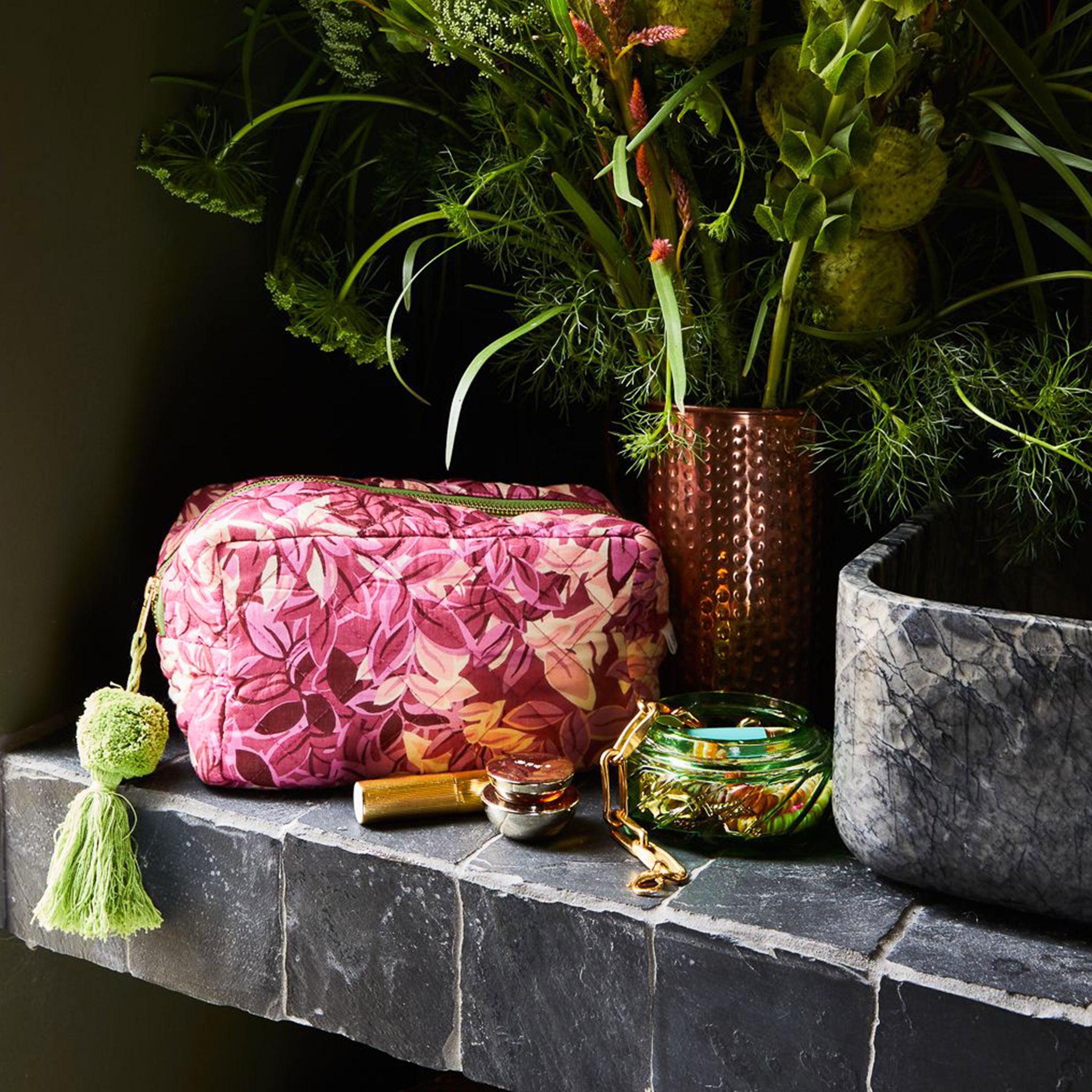 A pink floral patterned cosmetic bag with a green tassel zipper. 