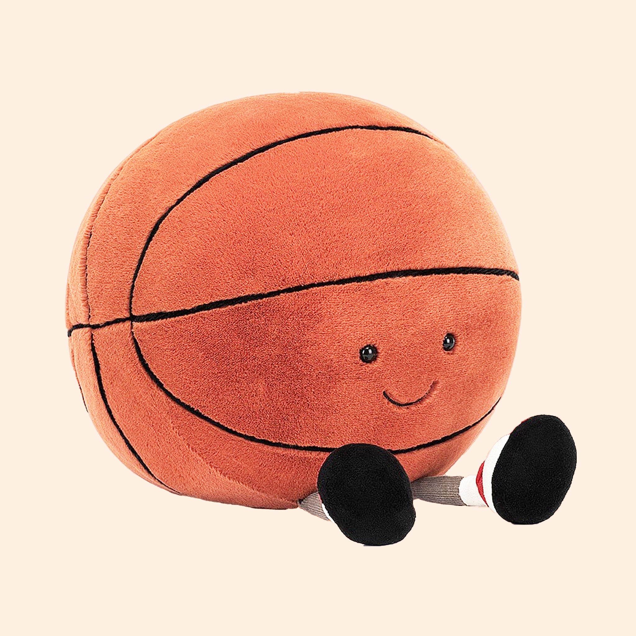 On an orange background is an orange basketball stuffed toy with a smiling face and feet.