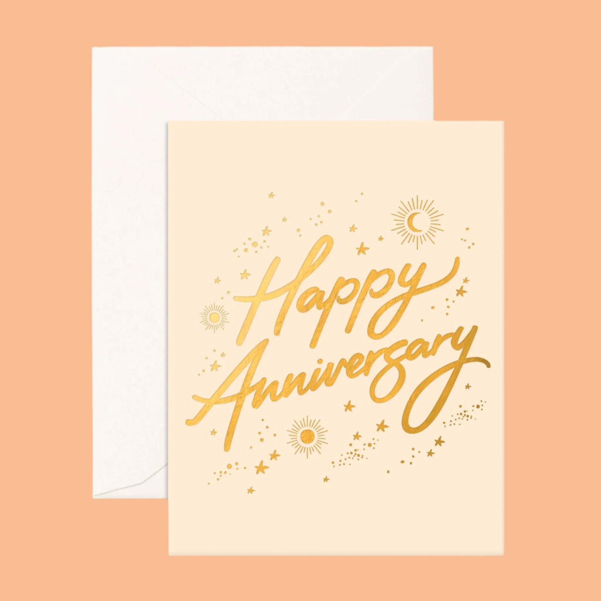 On a neutral background is a tan card with gold foil text that reads, &quot;Happy Anniversary&quot; along with gold foil stars, sun and moons around. 