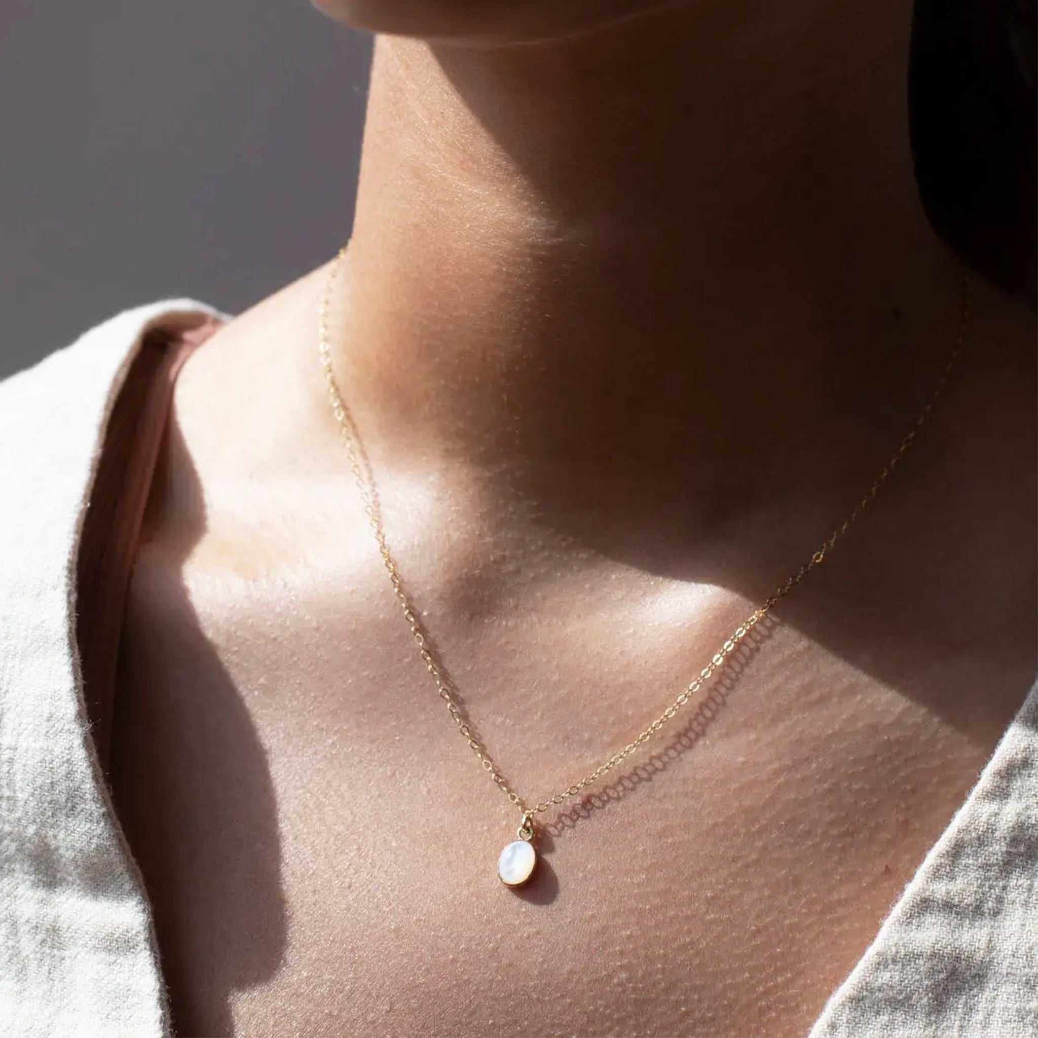 A gold chain necklace with a mother of pearl pendant.