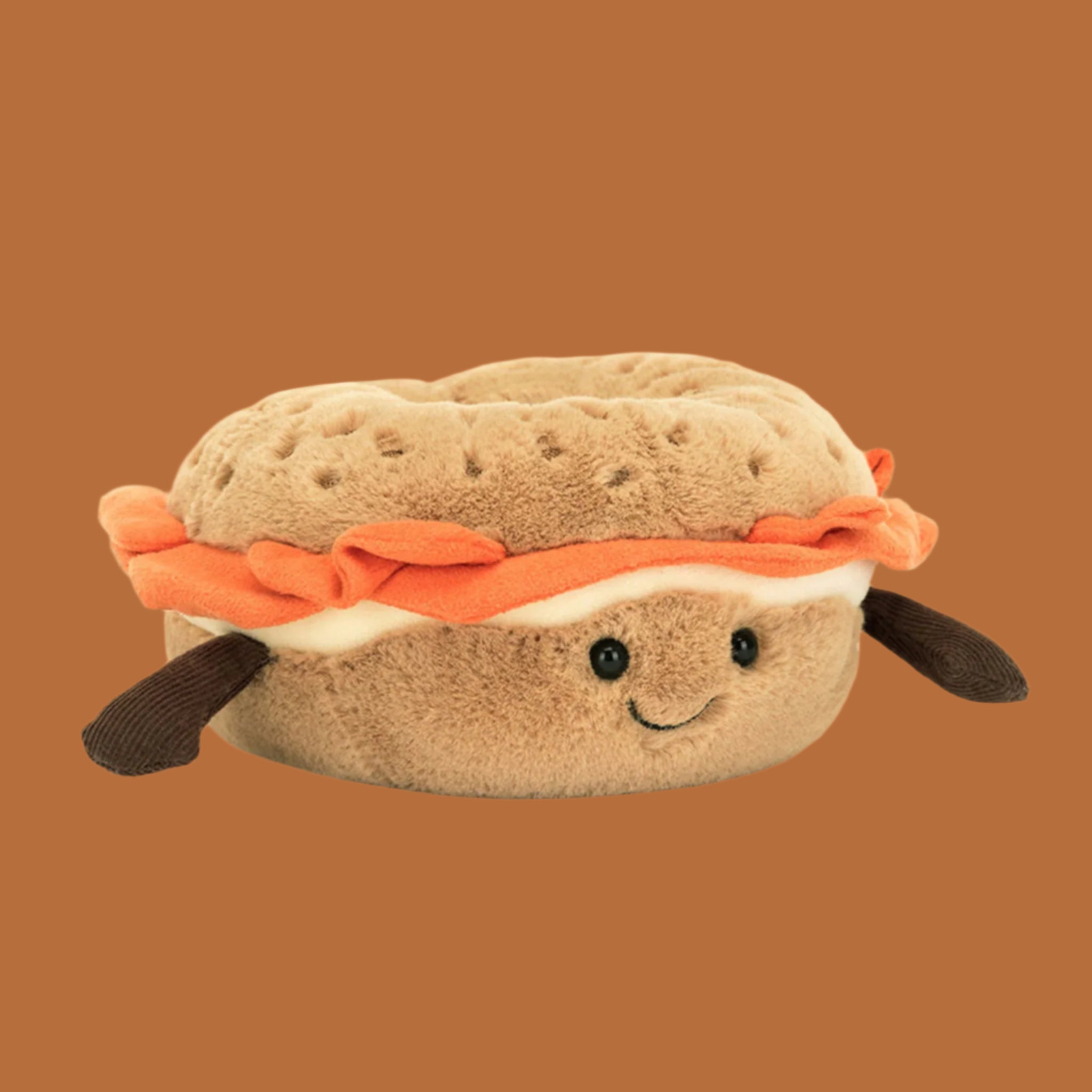 A bagel and lox shaped stuffed toy with a smiling face and arms. 