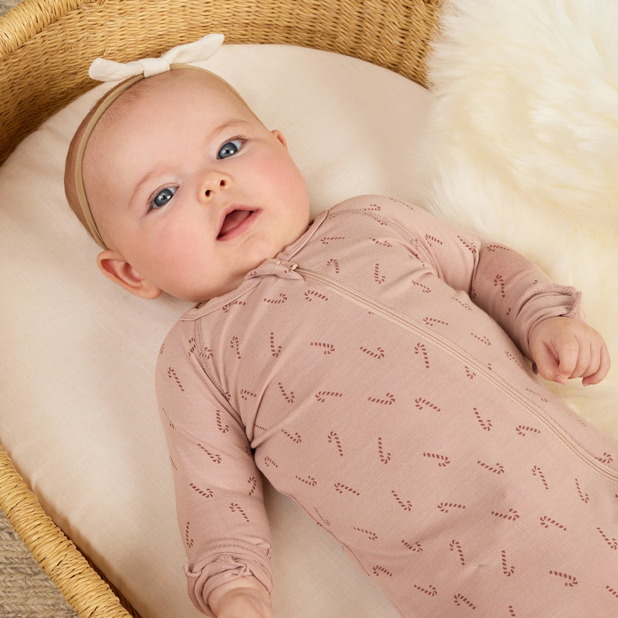 A light pink onesie with a front zipper and a candy cane print. 