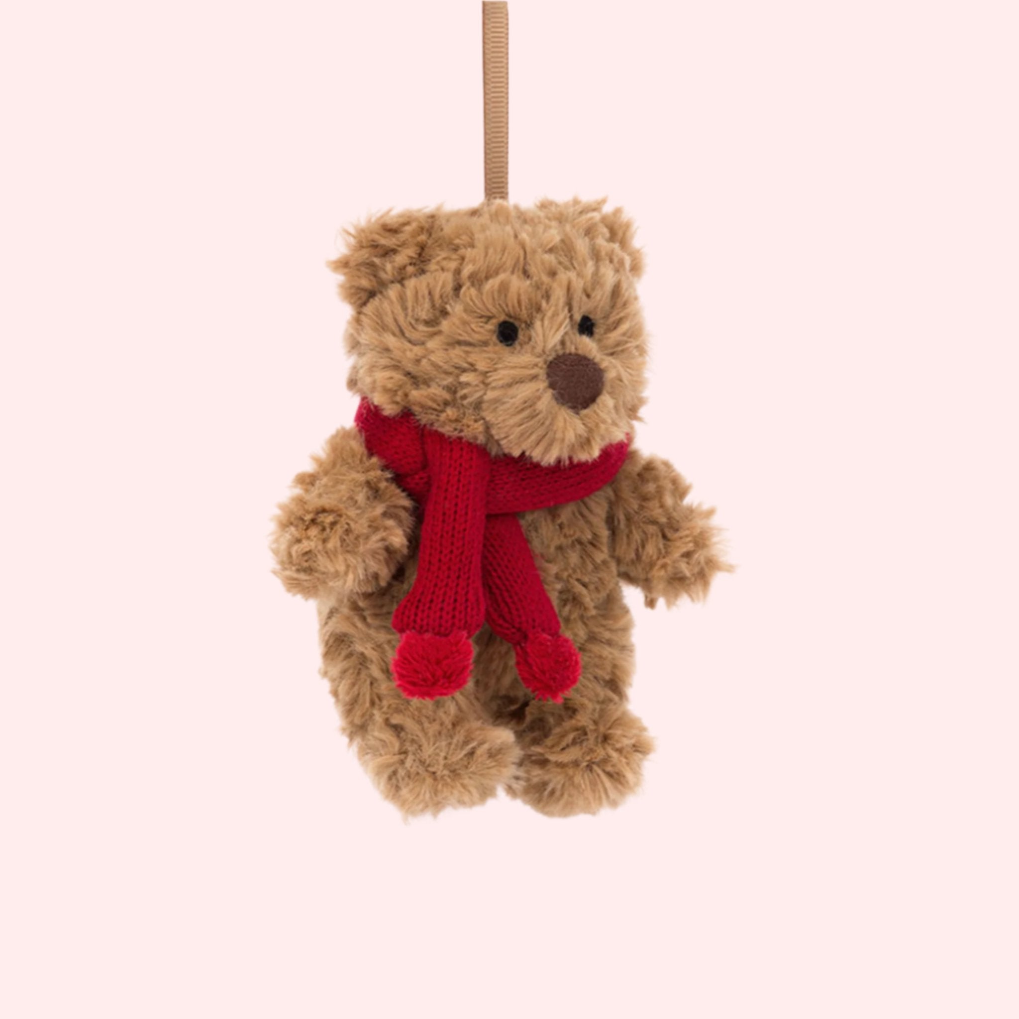 A brown small teddy bear shaped ornament wearing a red scarf. 