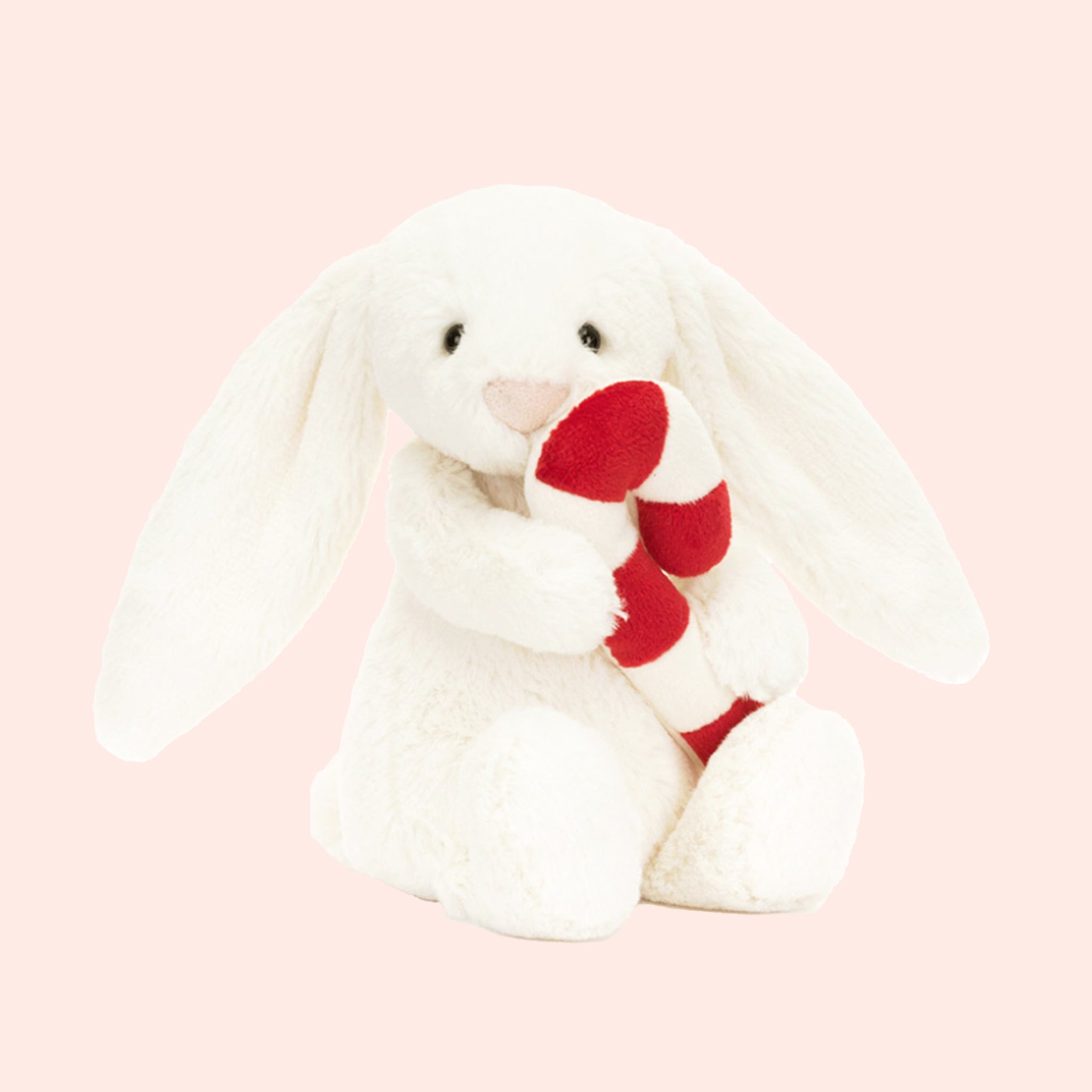 A white bunny shaped stuffed animal holding a red and white candy cane. 