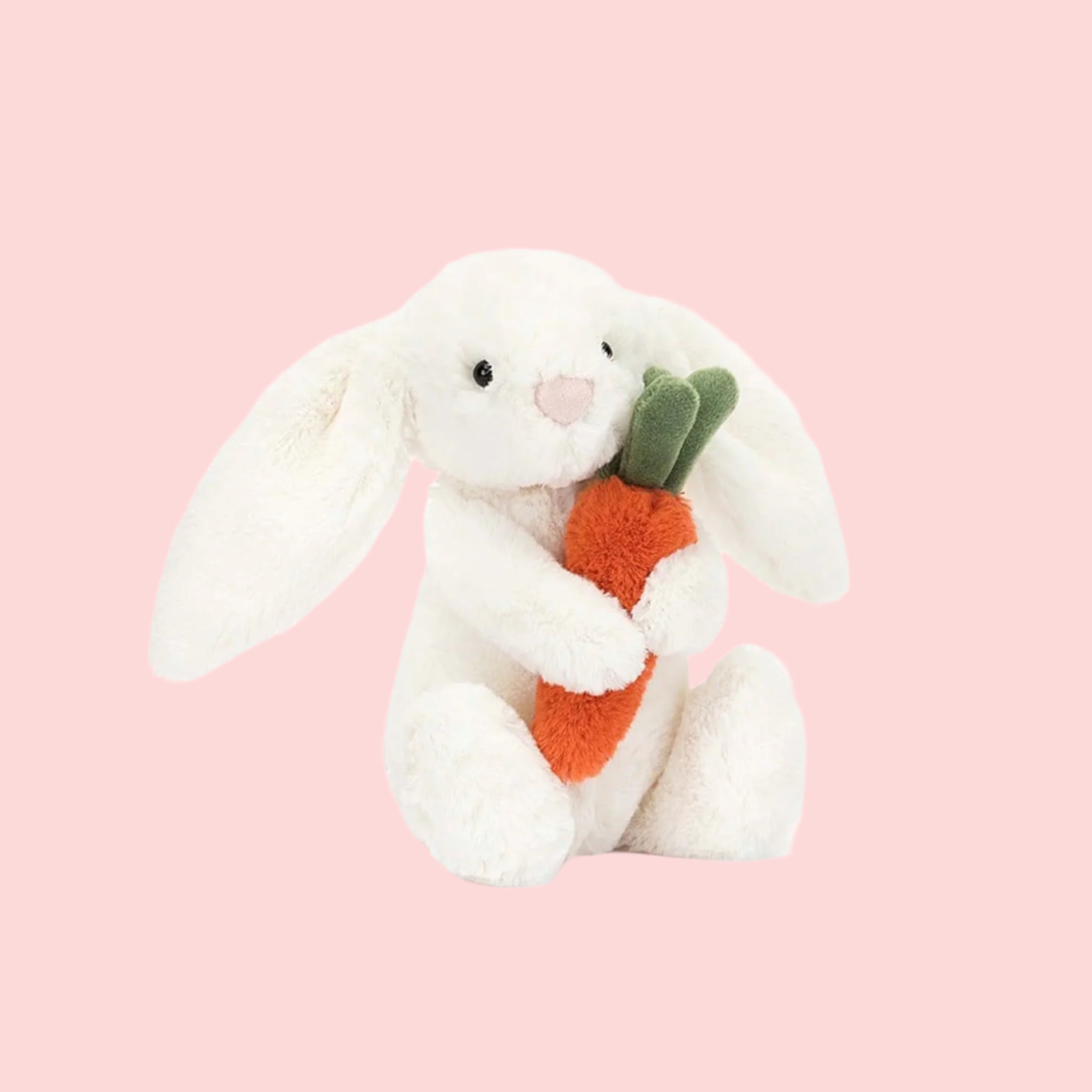 A white stuffed animal bunny holding an orange stuffed carrot. 