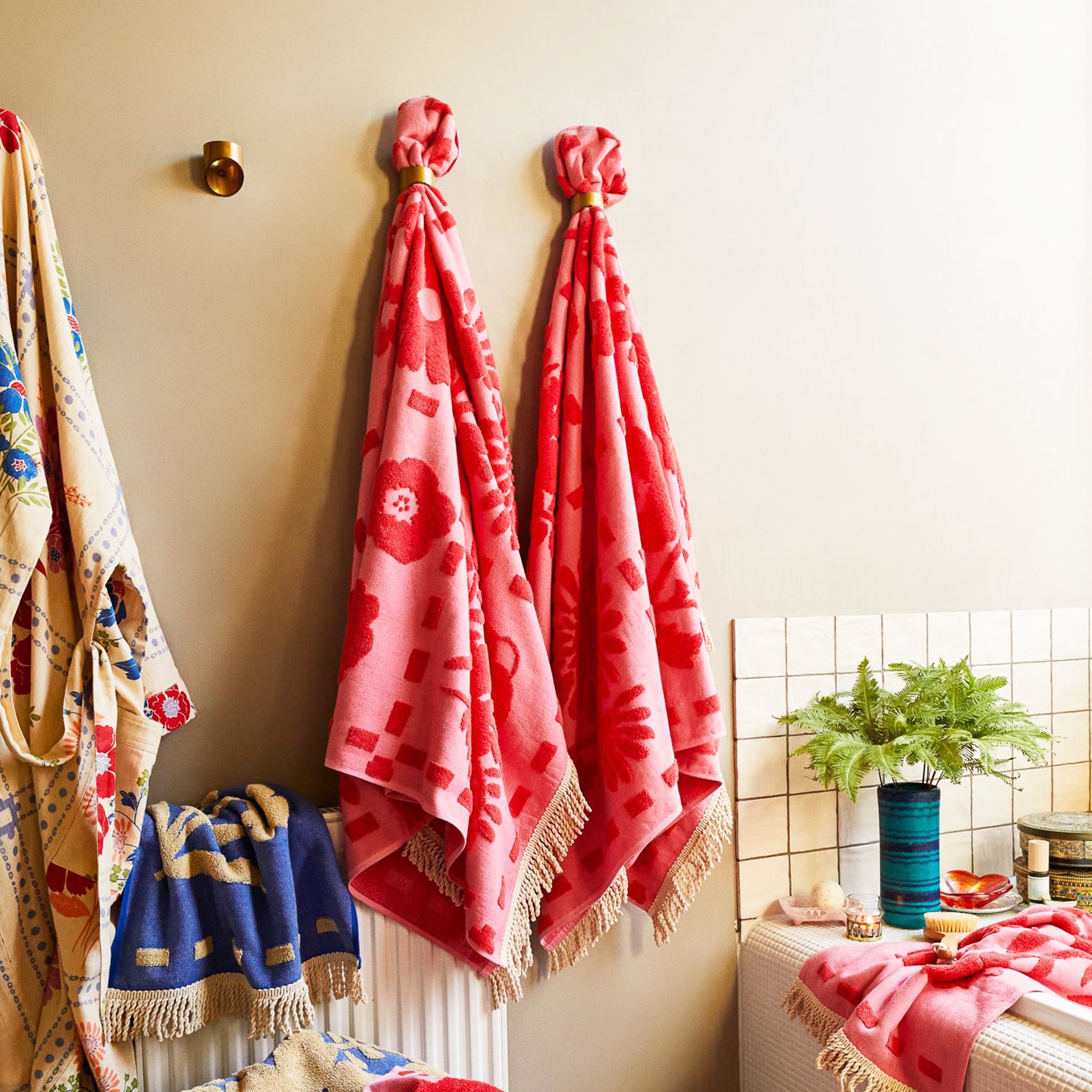 A pink bath towel with a floral print and fringe details on two edges. 