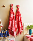 A pink bath towel with a floral print and fringe details on two edges. 