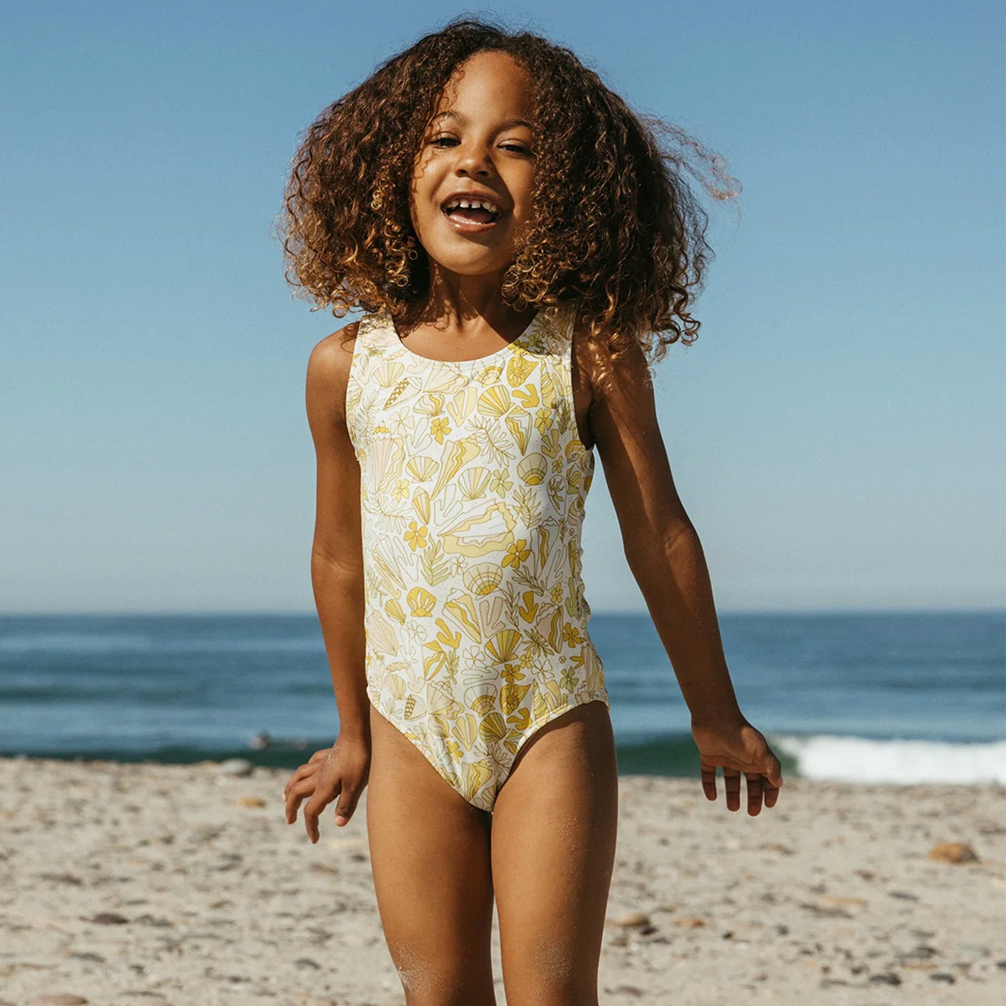 A yellow and white shell printed one piece swimsuit for children. 