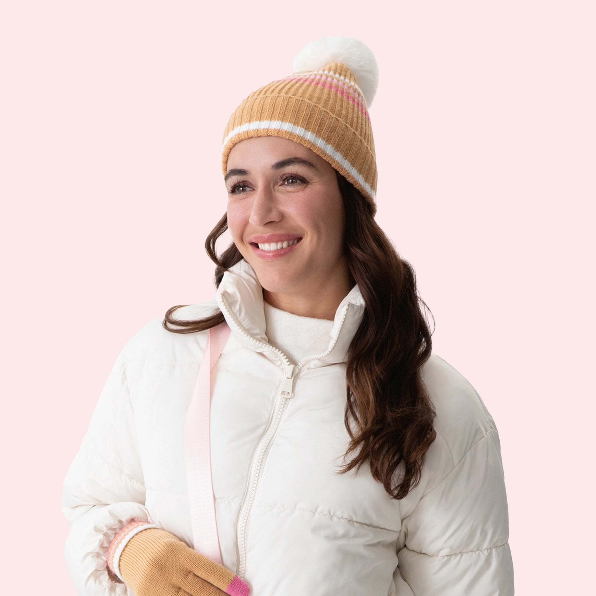 A tan beanie with a pink and white stripe pattern and a white pom pom puff at the top. 