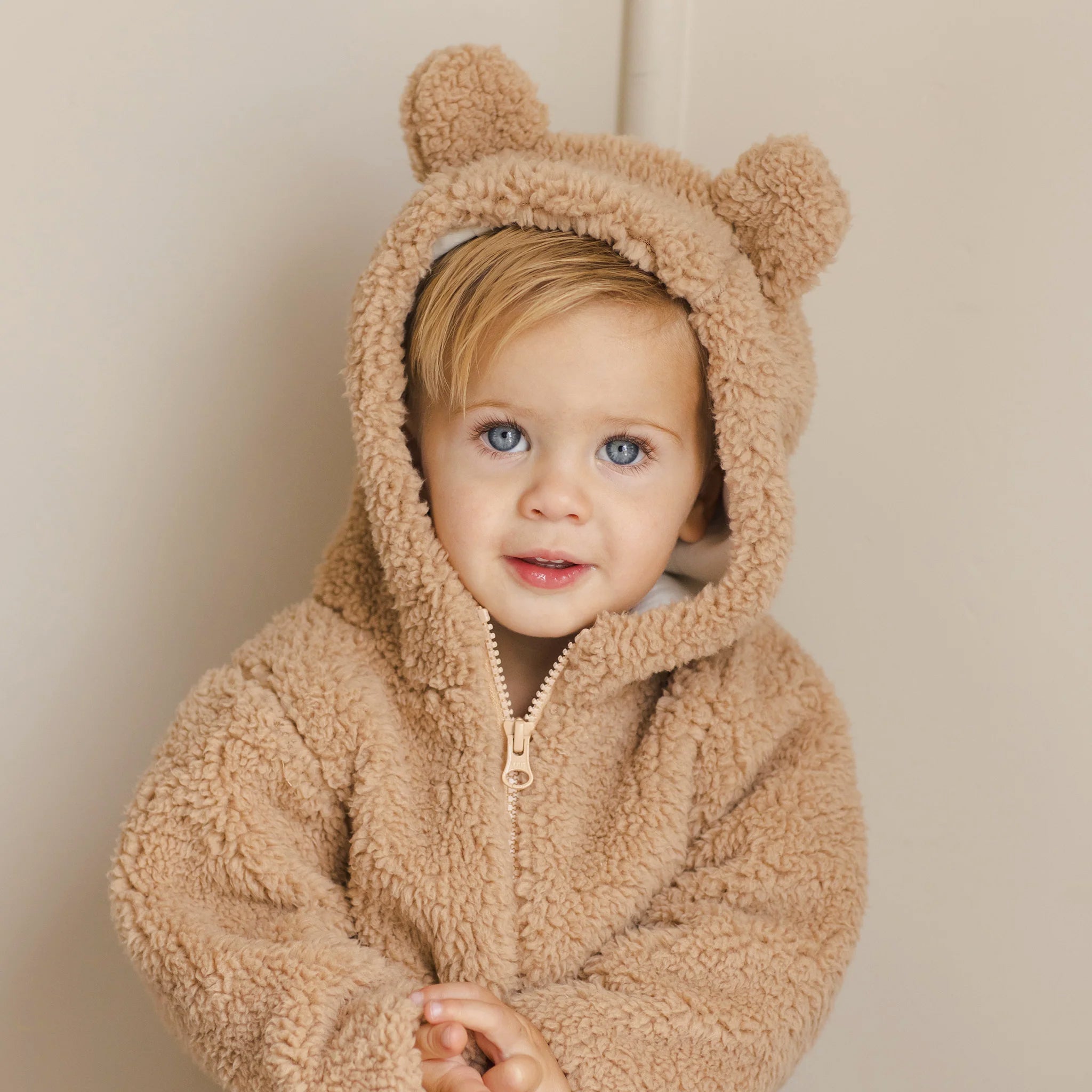 A beige fuzzy jacket with a bear hood with ears on the hood. 