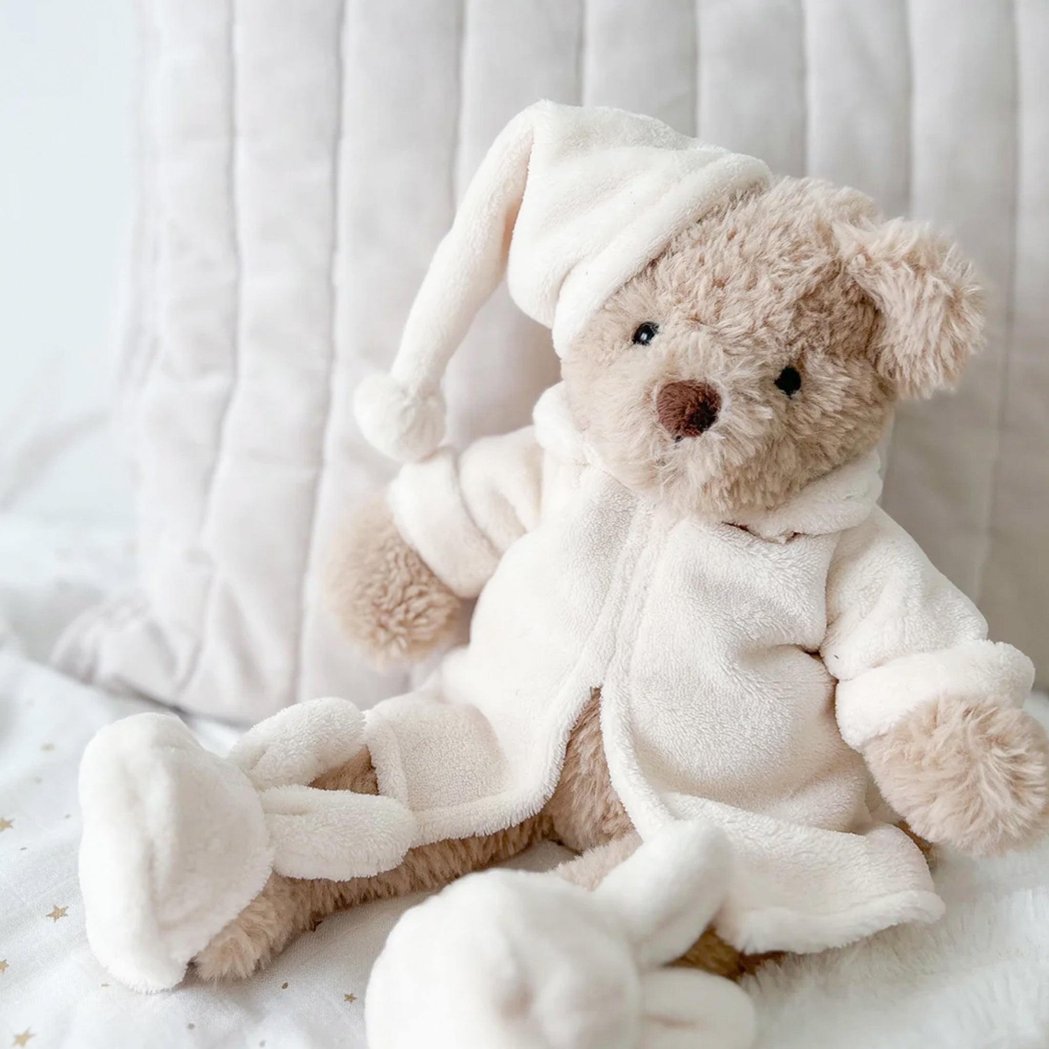 A bear stuffed animal wearing a white robe, night cap and bunny slippers. 