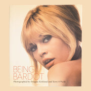 On a light tan background is an ivory book with a photo of Brigitte Bardot.  