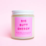 A clear glass candle with a pink label that reads, 'Big Butt Energy'. 