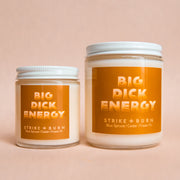 two glass candle vessels in a 4 ouch and 8 ouch size with white screw cap lid, white wax, and terracotta color sticker with "Big Dick Energy. Strike + Burn. Blue Spruce. Cedar. Fraser Fir" in peach font.