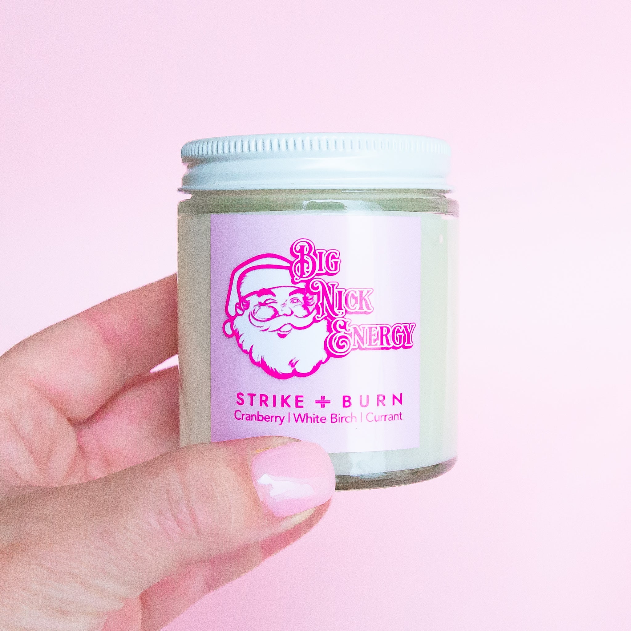 A clear glass jar candle with a pink label that reads, 'Big Nick Energy'. 