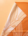 On an orange background is an orange kitchen towel with a white banana leaf design.