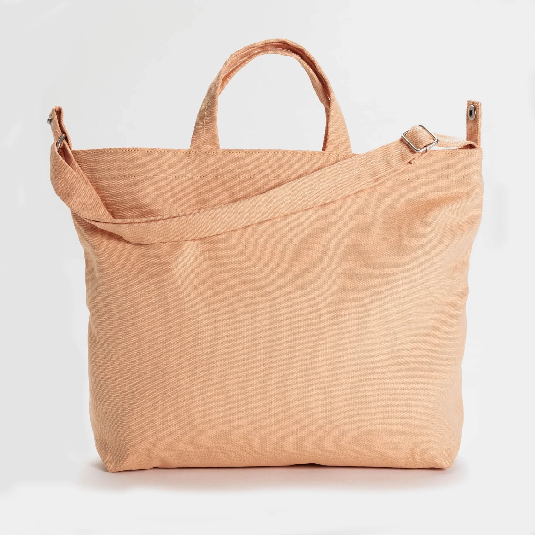 A square canvas tote bag with a zipper and two handles and a longer over the shoulder strap in a salmon color.