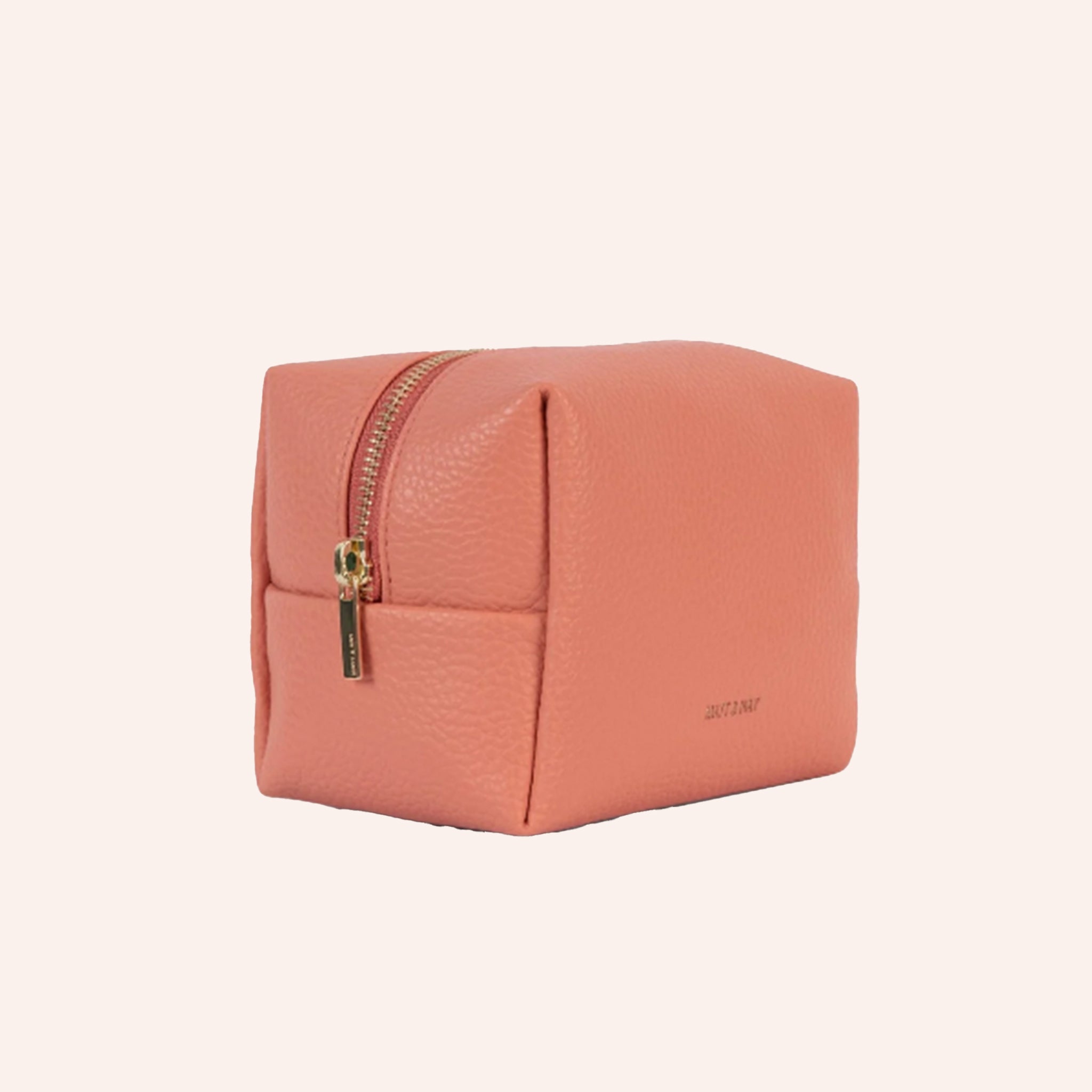 A coral vegan leather toiletry case with a handle on one side and a zipper closure across the top.