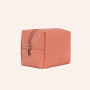 A coral vegan leather toiletry case with a handle on one side and a zipper closure across the top.