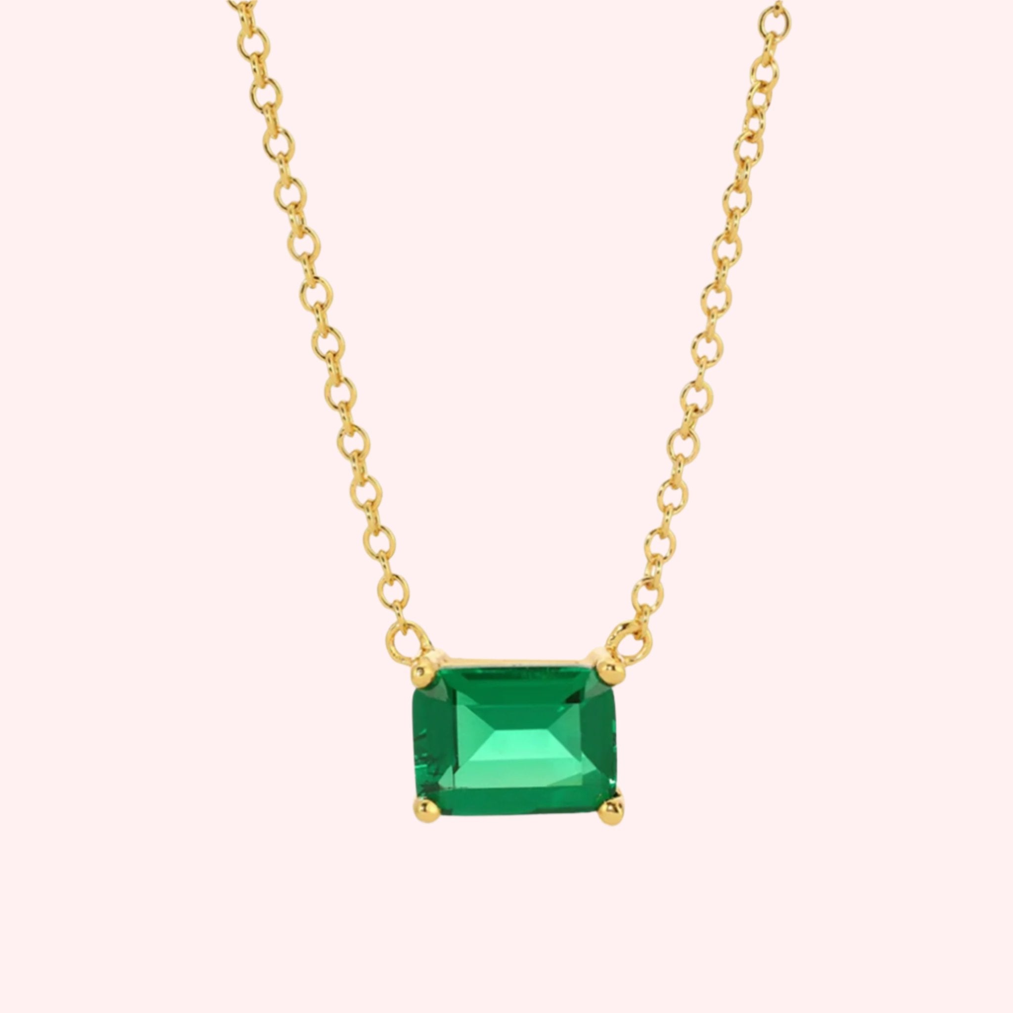 A gold chain necklace with a green emerald cut stone. 