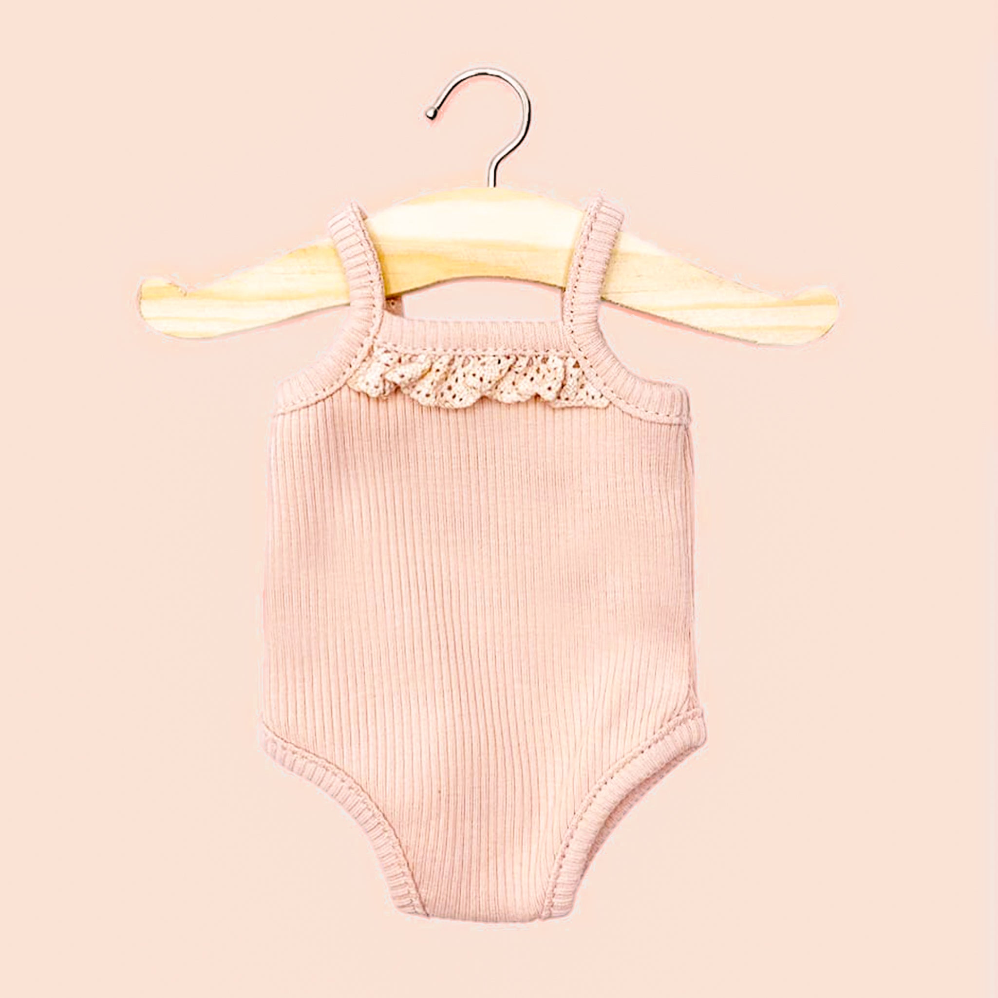 A darling pink bodysuit with ribbed fabric hangs on a tiny wooden hanger.  It's a doll's clothing.  The piece has a lace detail at the neck and is on a pink background.