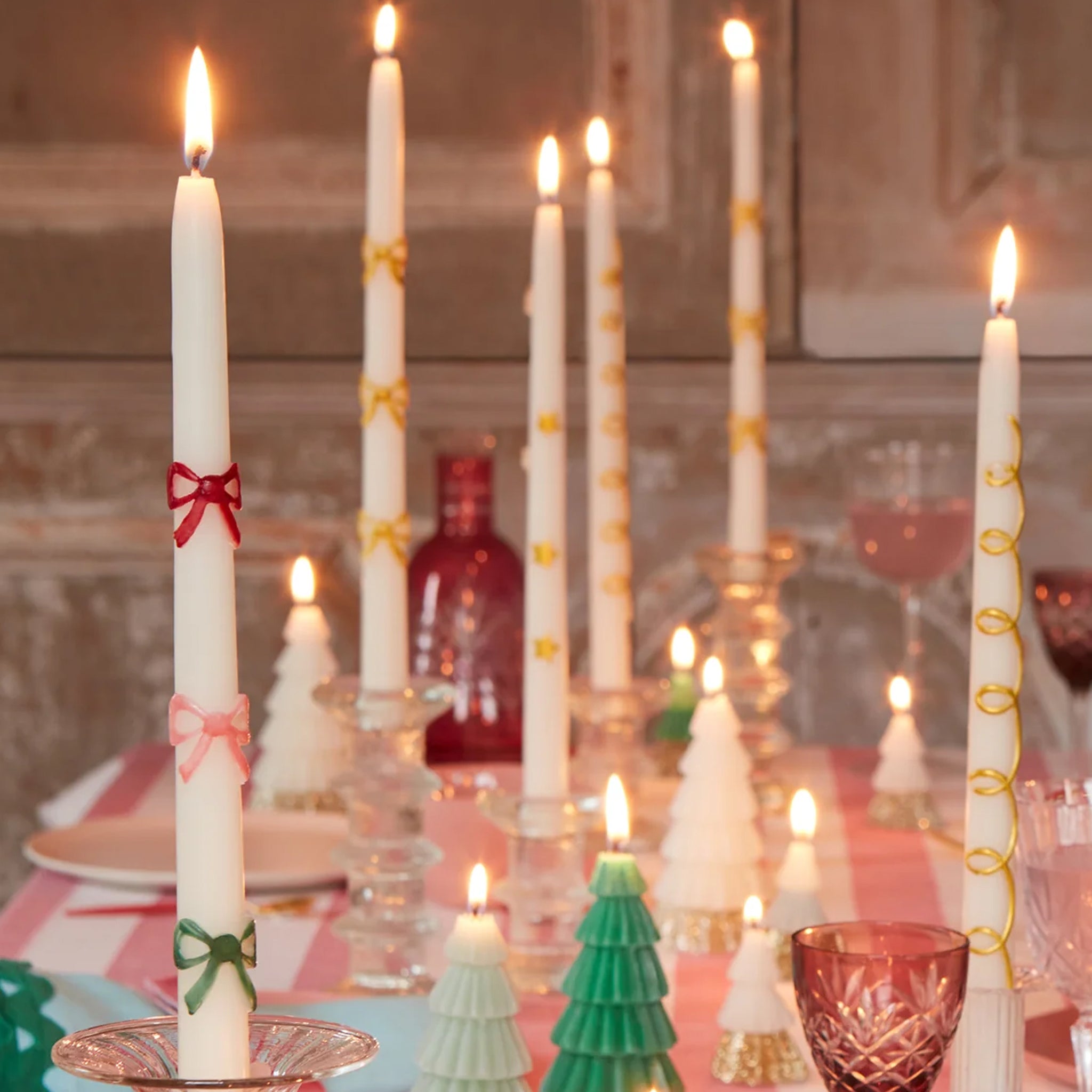 A set of two white taper candles with red, pink and green bow designs. 