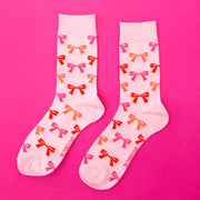 A pair of light pink socks with red, orange and pink bow patterns all over. 