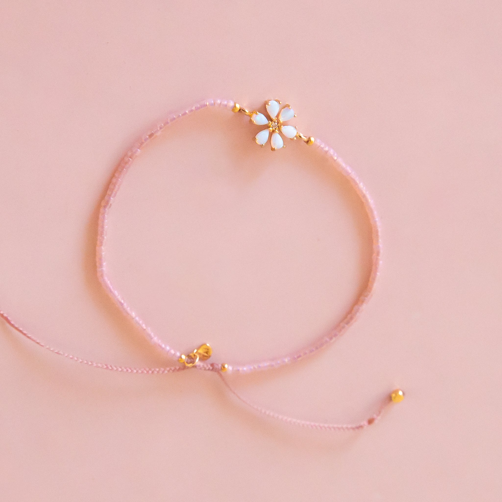 A pink and gold beaded bracelet with a opal flower design in the center. 