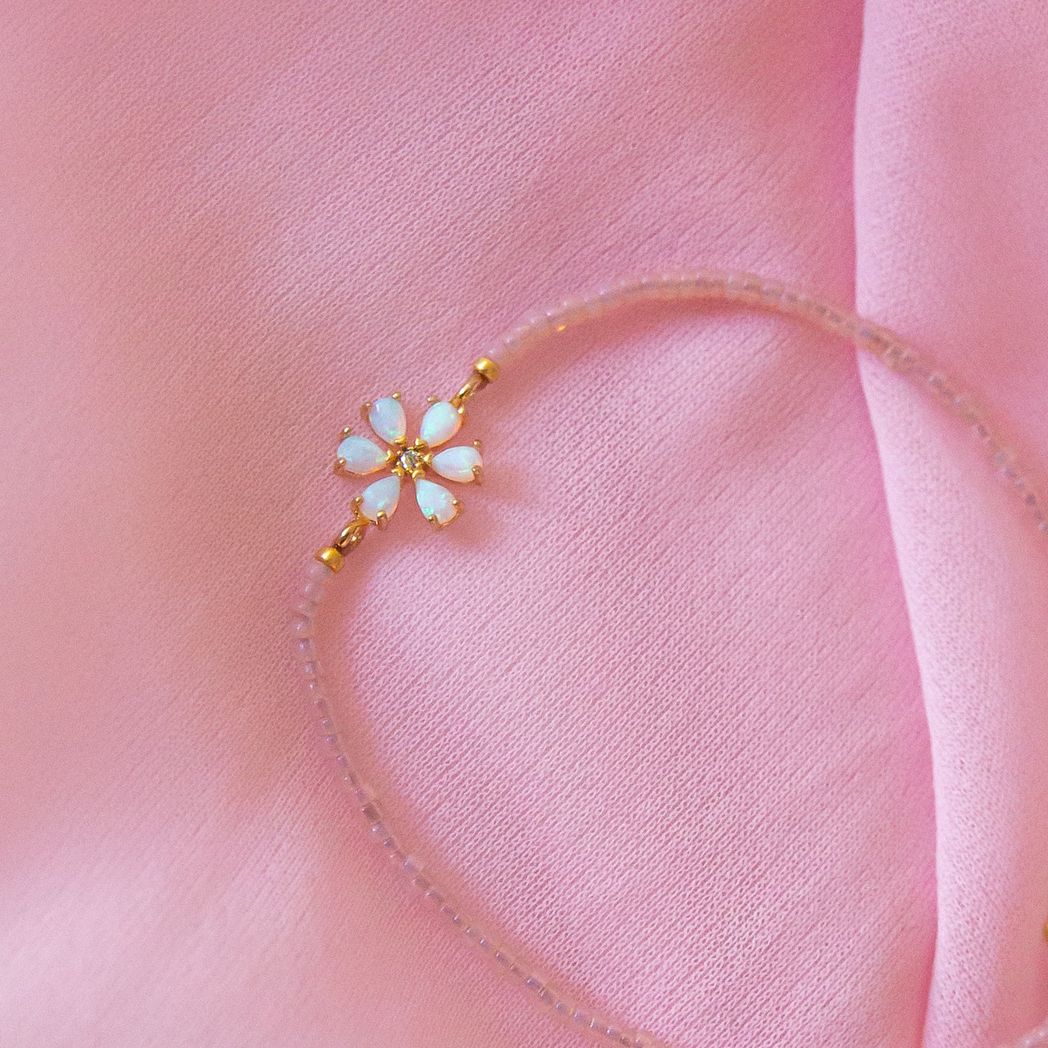 A pink and gold beaded bracelet with a opal flower design in the center. 