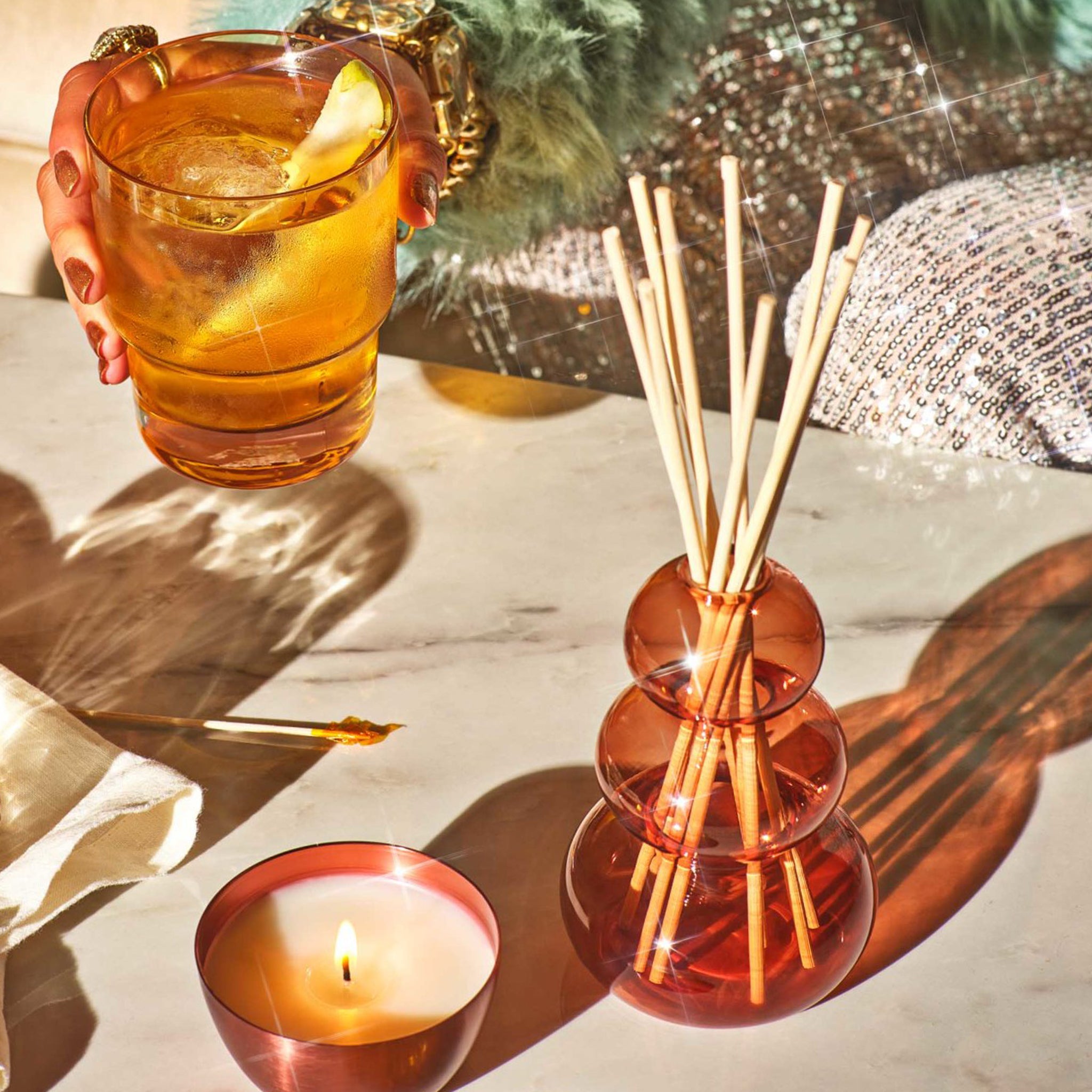 A reddish orange glass bubble shaped diffuser with wooden reeds. 