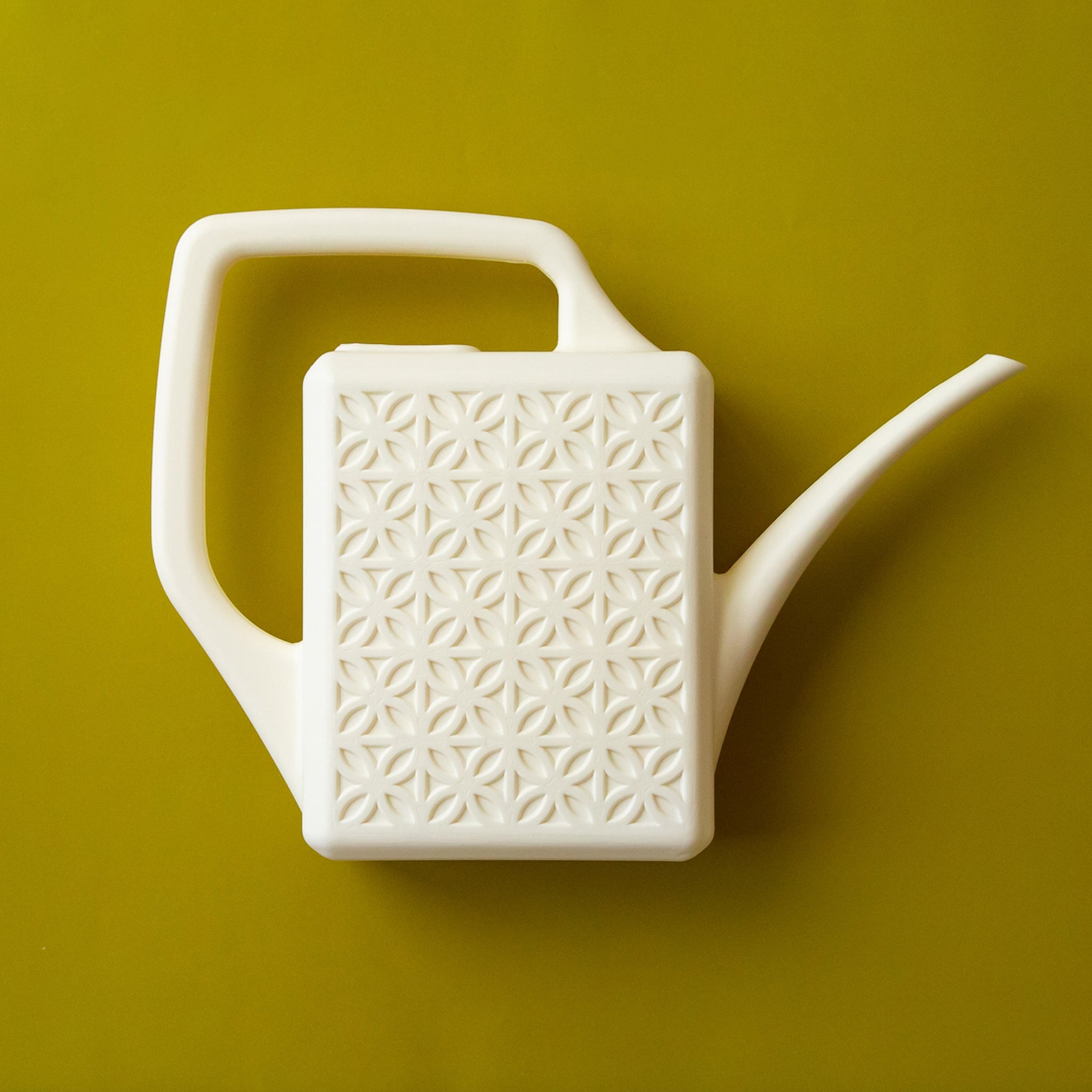 An ivory plastic watering can with a narrow spout and square handle and a rectangle breeze block design on the sides.