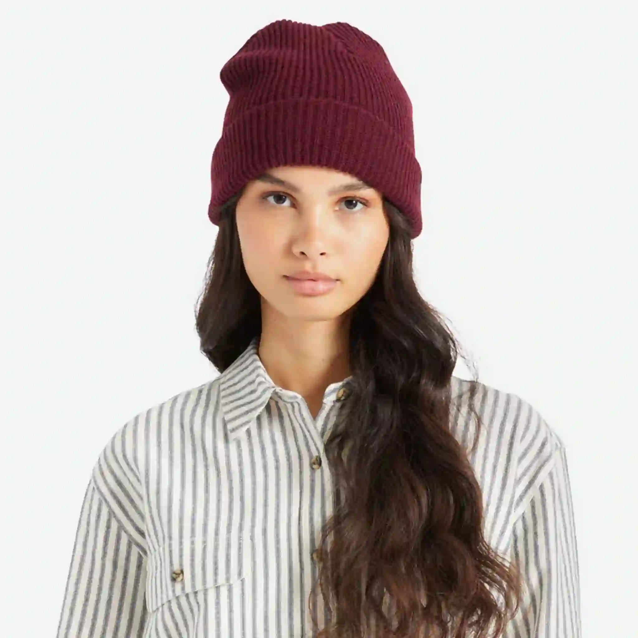 On a white background is a model wearing a mahogany colored knit beanie. 