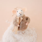 On a peachy background is a white felt mouse ornament with a brown jacket and brown skiis. 