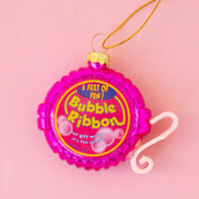 On a pink background is a bright pink Bubble Gum Tape Dispenser ornament with a gold loop for hanging.