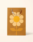 On a white background is a brown gift bag with a large yellow daisy in the center.