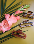 On a green background is a variety of rectangle claw clips in tortoise shades and an amber color.