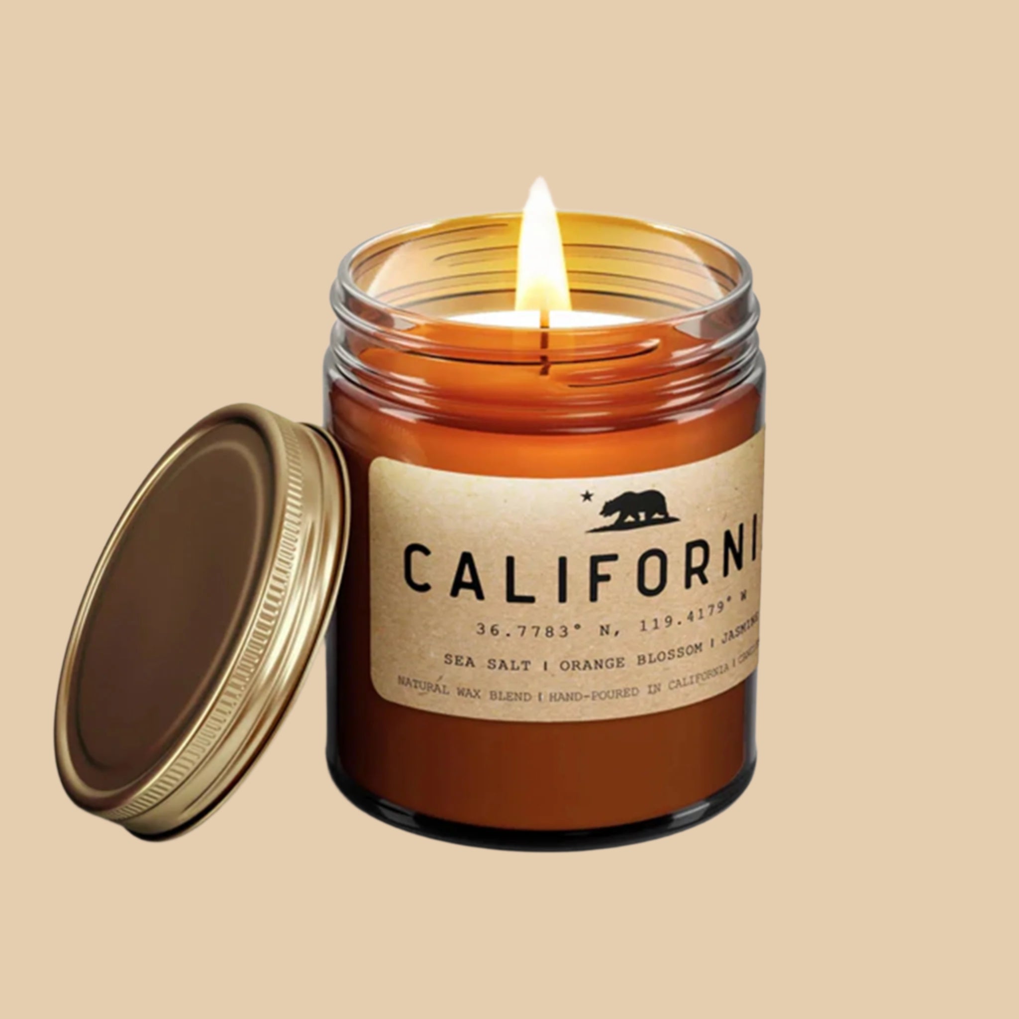 An amber glass jar candle with a light tan rectangular label that reads, "California Sea Salt | Orange Blossom | Jasmine |" in black letters along with a black filled in image of the California state bear and a gold screw on lid.