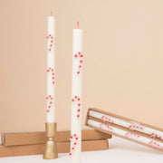 Two white taper candles with a red wick and red and white wax candy cane designs. 